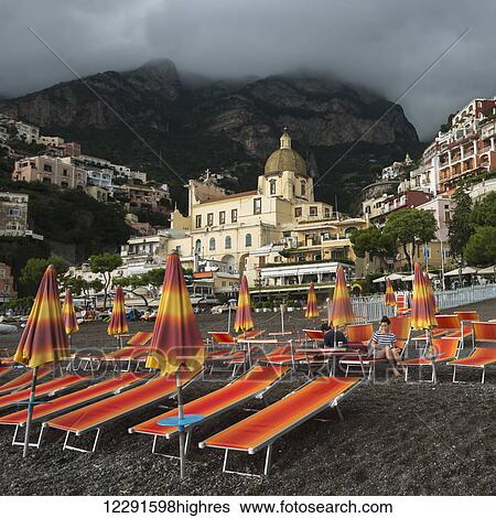 Stock Photograph - Colourful lounge chairs on the beach with buildings in the background along the Amalfi coast; Positano, Campania, Italy. Fotosearch