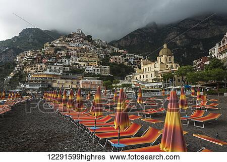 Stock Photograph - Colourful lounge chairs on the beach with houses on a hillside along the Amalfi coast; Positano, Campania, Italy. Fotosearch