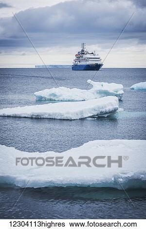 Stock Photograph - Cruise ship anchored with icebergs in foreground; Antarctica. Fotosearch