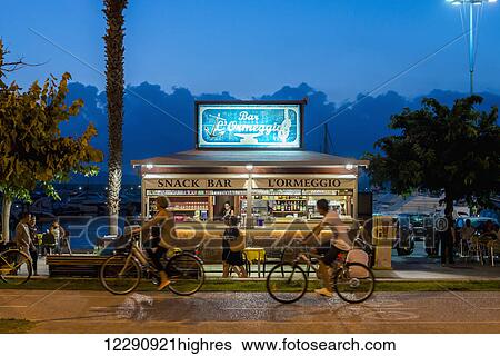 Stock Photograph - Cycling along the street at dusk; Alghero, Sardinia, Italy. Fotosearch