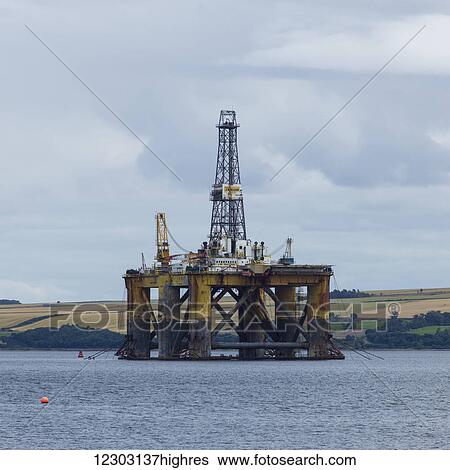 Stock Photograph - Drilling rig off the coast with farmland in the background; Invergorden, Scotland. Fotosearch