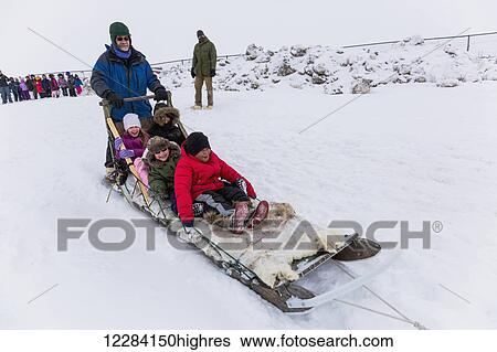 Stock Photograph - Elementary school children ride a sled pulled by sled dogs around the lagoon, Barrow, North Slope, Arctic Alaska, USA, Winter. Fotosearch