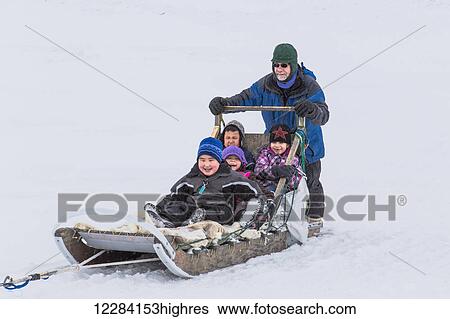 Stock Photograph - Elementary school children ride a sled pulled by sled dogs around the lagoon, Barrow, North Slope, Arctic Alaska, USA, Winter. Fotosearch