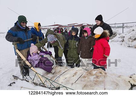 Stock Photograph - Elementary school kids wearing winter gear wait to ride a sled around the lagoon, Barrow, North Slope, Arctic Alaska, USA, Winter. Fotosearch