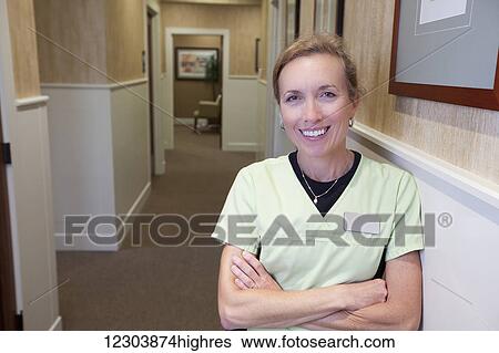 Female medical employee in an office corridor, leaning against the wall, looking at the camera with her arms crossed and a pleasant smile on her face; Bowling Green, Kentucky, United States of America View Large Photo Image Stock Photograph - Female medical employee in an office corridor, leaning against the wall, looking at the camera with her arms crossed and a pleasant smile on her face; Bowling Green, Kentucky, United States of America. Fotosearch