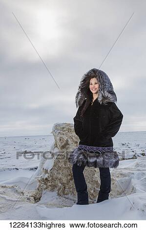 Stock Photograph - Female native youth wearing a traditional fur parka while standing on ice along the Arctic Ocean, Barrow, North Slope, Arctic Alaska, USA, Winter. Fotosearch
