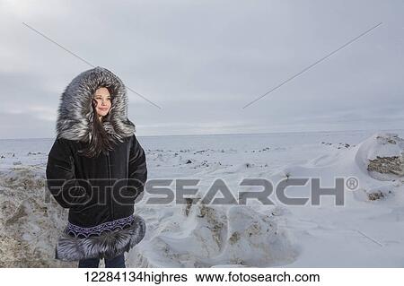 Stock Photograph - Female native youth wearing a traditional fur parka while standing on ice along the Arctic Ocean, Barrow, North Slope, Arctic Alaska, USA, Winter. Fotosearch