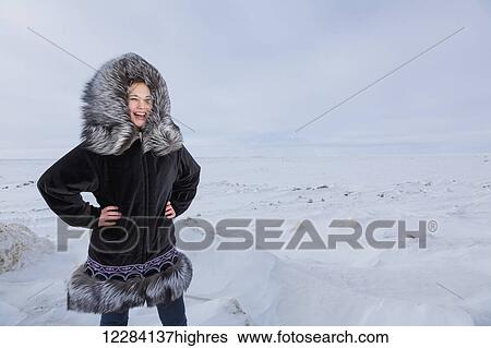 Stock Photograph - Female native youth wearing a traditional fur parka while standing on ice along the Arctic Ocean, Barrow, North Slope, Arctic Alaska, USA, Winter. Fotosearch