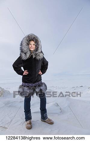 Stock Photograph - Female native youth wearing a traditional fur parka while standing on ice along the Arctic Ocean, Barrow, North Slope, Arctic Alaska, USA, Winter. Fotosearch