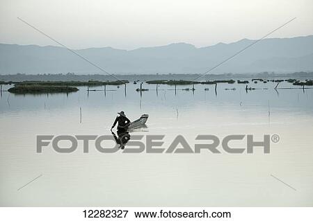 Stock Photo - Fisherman in a pirogue at sunset on Phayao Lake; Phayao, Thailand. Fotosearch