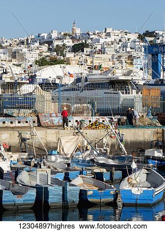 Stock Photograph - Fishing boats in the port with whitewash buildings on the hillside; Tangier, Morocco. Fotosearch
