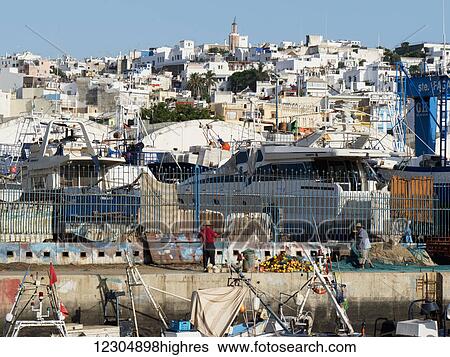 Stock Photograph - Fishing boats in the port with whitewash buildings on the hillside; Tangier, Morocco. Fotosearch