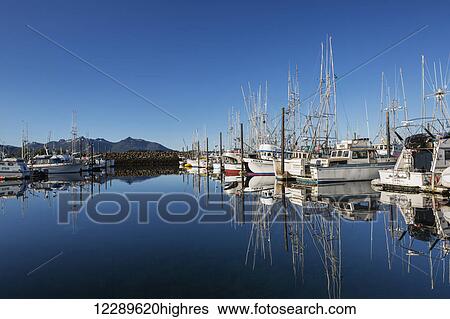Stock Photograph - Fishing boats reflect in the calm waters in the Sitka Harbor, clear skies in the background, Sitka, Southeast Alaska, USA, Summer. Fotosearch