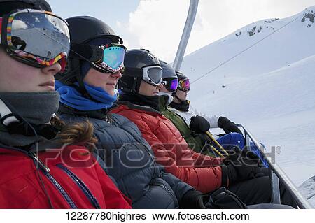 Stock Photograph - Five skiers in helmets and masks sitting on a chairlift at a ski resort; Whistler, British Columbia, Canada. Fotosearch