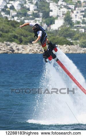 Stock Photograph - Flyboarder diving into water from great height; Torba, Mugla Province, Turkey. Fotosearch