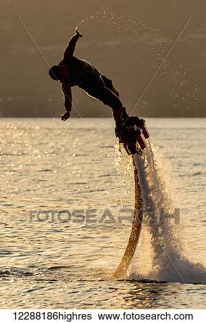 Flyboarder in silhouette leans into dive, trailing water droplets from his hand; Torba, Mugla Province, Turkey View Large Photo Image Stock Photograph - Flyboarder in silhouette leans into dive, trailing water droplets from his hand; Torba, Mugla Province, Turkey. Fotosearch