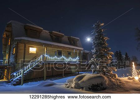 Stock Photograph - Full moon and holiday lights brighten up a wintery night at a log home in Anchorage, South-central Alaska. Fotosearch