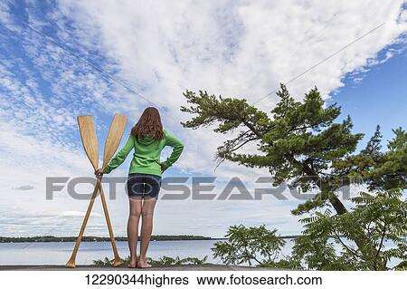 Stock Photograph - Girl holding paddles overlooking Balsam Lake; Ontario, Canada. Fotosearch