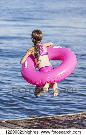 Stock Photograph - Girl jumping off a dock by Balsam Lake wearing inflatable ring; Ontario, Canada. Fotosearch