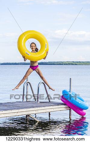 Girl jumping on dock by Balsam Lake holding a yellow inflatable ring; Ontario, Canada View Large Photo Image Stock Photograph - Girl jumping on dock by Balsam Lake holding a yellow inflatable ring; Ontario, Canada. Fotosearch