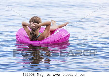 Stock Photograph - Girl resting in pink inflatable ring on Balsam Lake; Ontario, Canada. Fotosearch