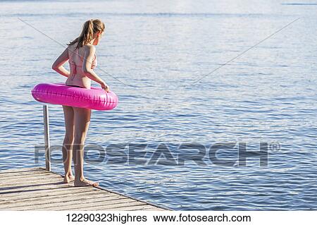 Stock Photograph - Girl standing on edge of dock by Balsam Lake wearing inflatable ring; Ontario, Canada. Fotosearch