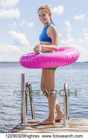 Stock Photograph - Girl standing on edge of dock by Balsam Lake wearing inflatable ring; Ontario, Canada. Fotosearch