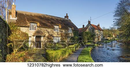 Stock Photograph - Houses and a path along a river; Thornton Le Dale, North Yorkshire, England. Fotosearch