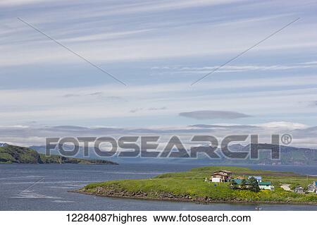 Stock Photograph - Houses on a small peninsula with mountains and ocean in the background, Sand Point, Southwestern Alaska, USA, Summer. Fotosearch