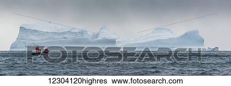 Stock Photograph - Inflatable cruises towards blue iceberg on horizon; Antarctica. Fotosearch