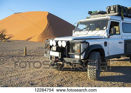 Picture - Land Rover Defender 110 parked in the desert with dunes in the distance; Sossusvlei, Namibia. Fotosearch