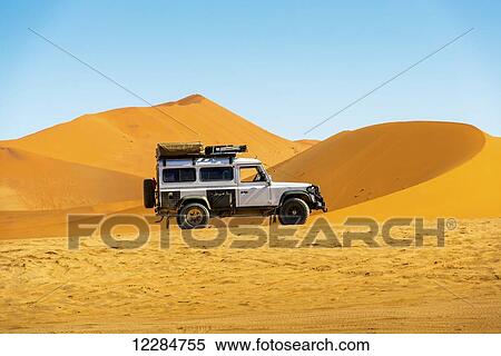 Stock Photography - Land Rover Defender 110 parked in the desert with dunes in the distance; Sossusvlei, Namibia. Fotosearch