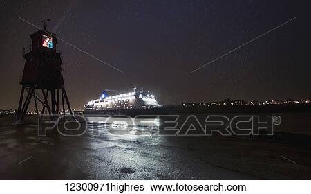 Stock Photograph - Light streaming from a lighthouse on the coast as an illuminated cruise ship passes by; South Shields, Tyne and Wear, England. Fotosearch