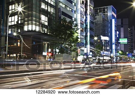 Stock Image - Light trails on a street with illuminated buildings at nighttime; Tokyo, Japan. Fotosearch