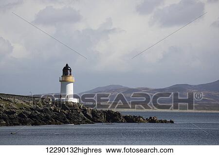 Stock Photograph - Lighthouse at the water's edge under a cloudy sky; Port Charlotte, Isle of Islay, Scotland. Fotosearch