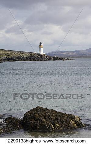 Stock Photograph - Lighthouse at the water's edge under a cloudy sky; Port Charlotte, Isle of Islay, Scotland. Fotosearch