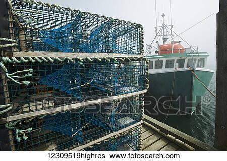 Stock Photograph - Lobster traps on wharf by fishing boat; Cape Forchu, Nova Scotia, Canada. Fotosearch