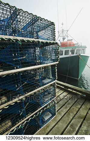 Stock Photograph - Lobster traps on wharf by fishing boat; Cape Forchu, Nova Scotia, Canada. Fotosearch