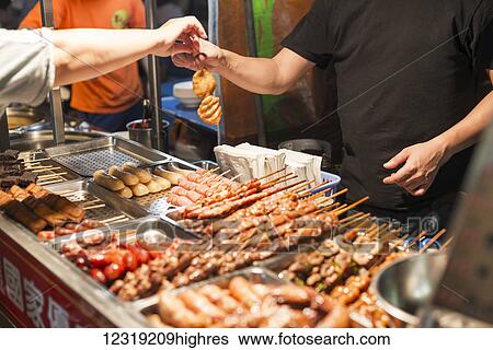 Stock Photograph - Local night markets of Taipei are really famous because it's delicious food, vendor giving out barbequed skewers; Taiwan, China. Fotosearch