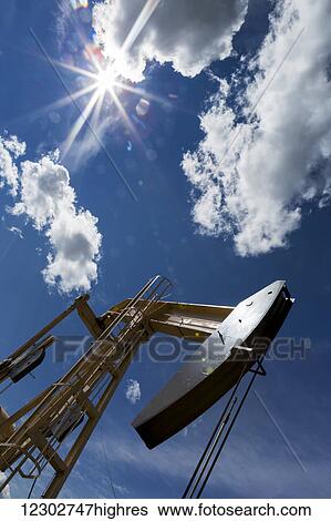 Low angle view of a pump jack with a sun burst in the blue sky and large puffy clouds; Alberta, Canada View Large Photo Image Stock Photograph - Low angle view of a pump jack with a sun burst in the blue sky and large puffy clouds; Alberta, Canada. Fotosearch