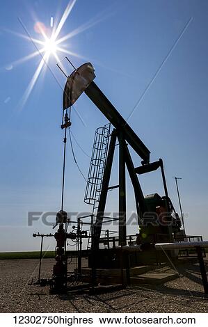 Stock Photograph - Low angle view of a pump jack with a sun burst in the blue sky; Acme, Alberta, Canada. Fotosearch