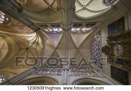 Stock Photograph - Low angle view of an ornate ceiling with stained glass windows and a clock; Toledo, Castile-La Mancha, Spain. Fotosearch