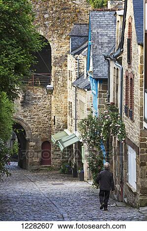 Male walking down a cobblestone road framed with old stone buildings and stone wall in the distance; Dinan, Brittany, France View Large Photo Image Stock Photo - Male walking down a cobblestone road framed with old stone buildings and stone wall in the distance; Dinan, Brittany, France. Fotosearch
