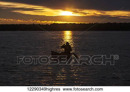 Stock Photograph - Man paddling canoe at sunrise on Balsam Lake; Ontario, Canada. Fotosearch