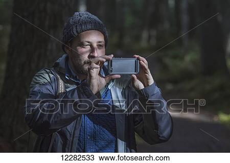 Stock Image - Man photographing the forest around Girdwood with his smartphone, Southcentral Alaska.. Fotosearch
