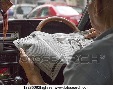 Stock Photograph - Man reading a newspaper in the drivers seat of a car; Bangkok, Thailand. Fotosearch