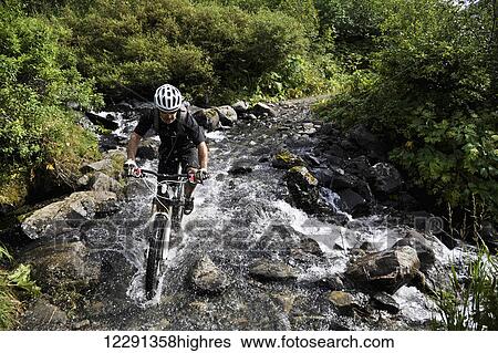 Stock Photograph - Man rides a full suspension mountain bike across a stream on the Devil's Pass Trail in the Chugach National Forest, Kenai Peninsula, South-central Alaska. Fotosearch