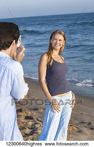 Stock Photograph - Man taking a photograph of a woman on the beach; Los Angeles, California, United States of America. Fotosearch