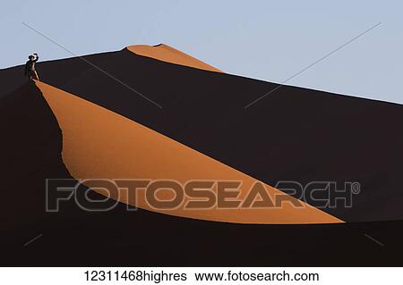Stock Photograph - Man taking a selfie of himself while walking the sand dunes of the Namib desert in Sossusvlei; Namibia. Fotosearch