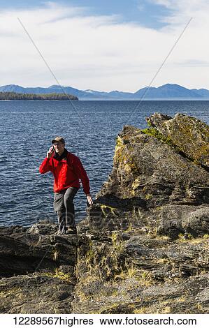 Stock Photograph - Man talks on his smart phone along the rocky shores of Tongass Narrows, Ketchikan, Southeast Alaska, Spring. Fotosearch